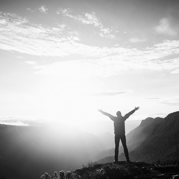 A young person outstretches their arms in the morning sun while hiking in the mountains