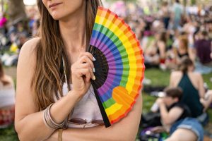 Person holding a rainbow-coloured hand fan at an outdoor Pride festival