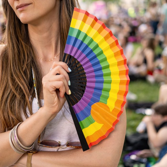Person holding a rainbow-coloured hand fan at an outdoor Pride festival