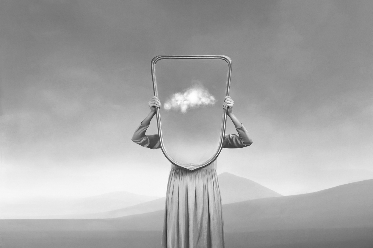 A person in a dress hides behind a mirror
