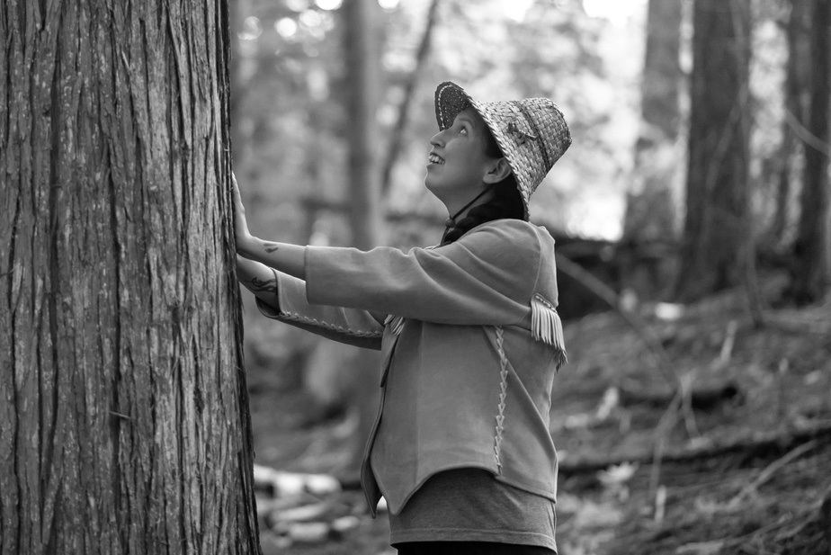 An indigenous woman places her hands onto the bark of a cedar tree