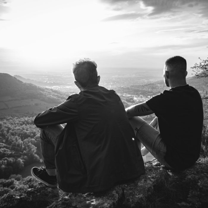 Two people sit together on a mountain peak