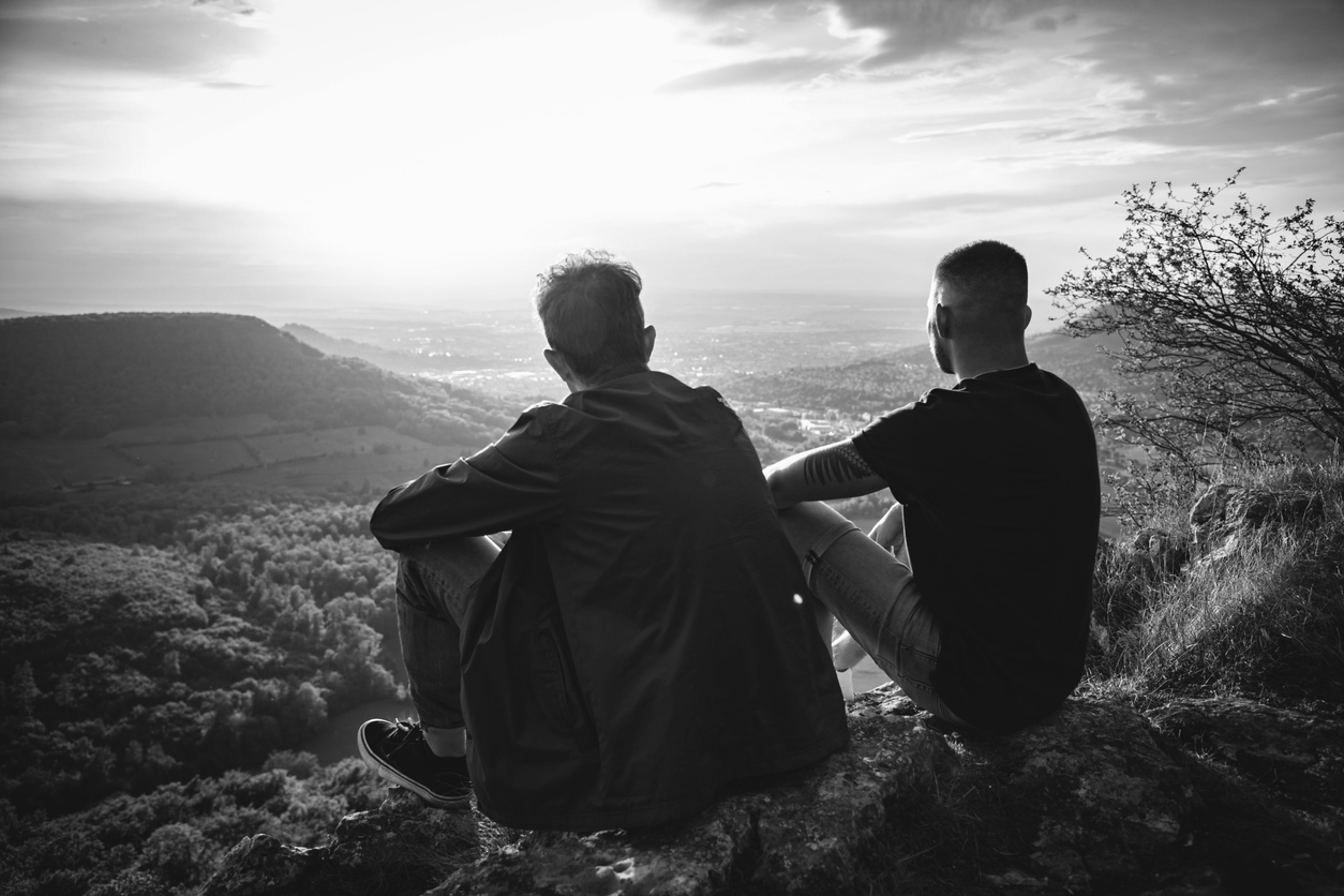Two people sit together on a mountain peak