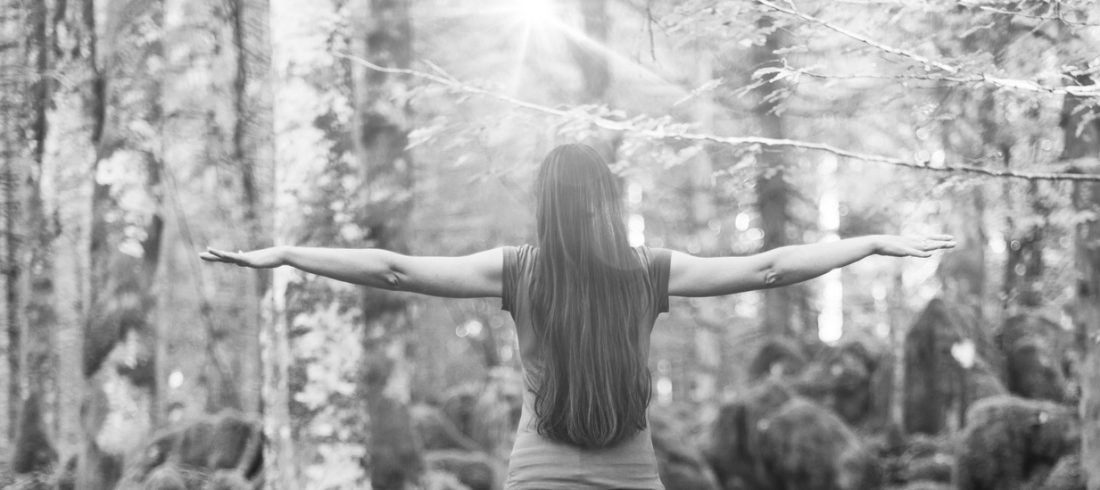 Person stands with outstretched arms, surrounded by forest