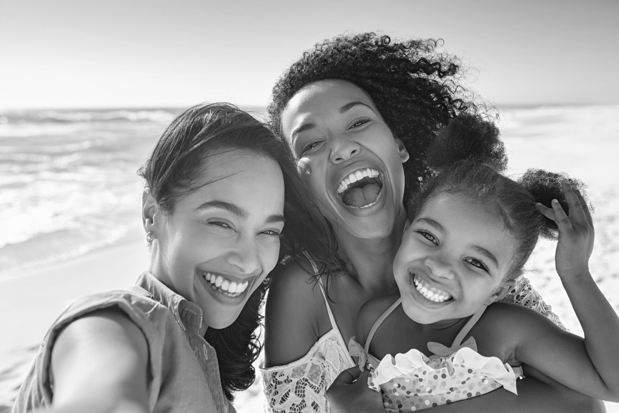 Queer family of colour smiling together at the beach